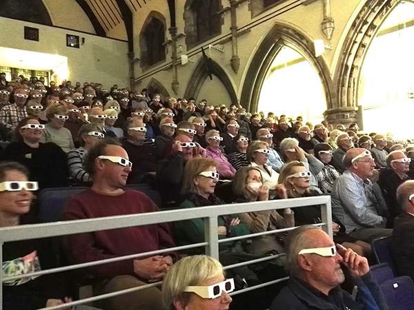  An image of  society members looking taken at the the font of the lecture theatre. The audience are wearing cardboard framed stereo glasses to see  a stereo anaglyph projection in 3D.